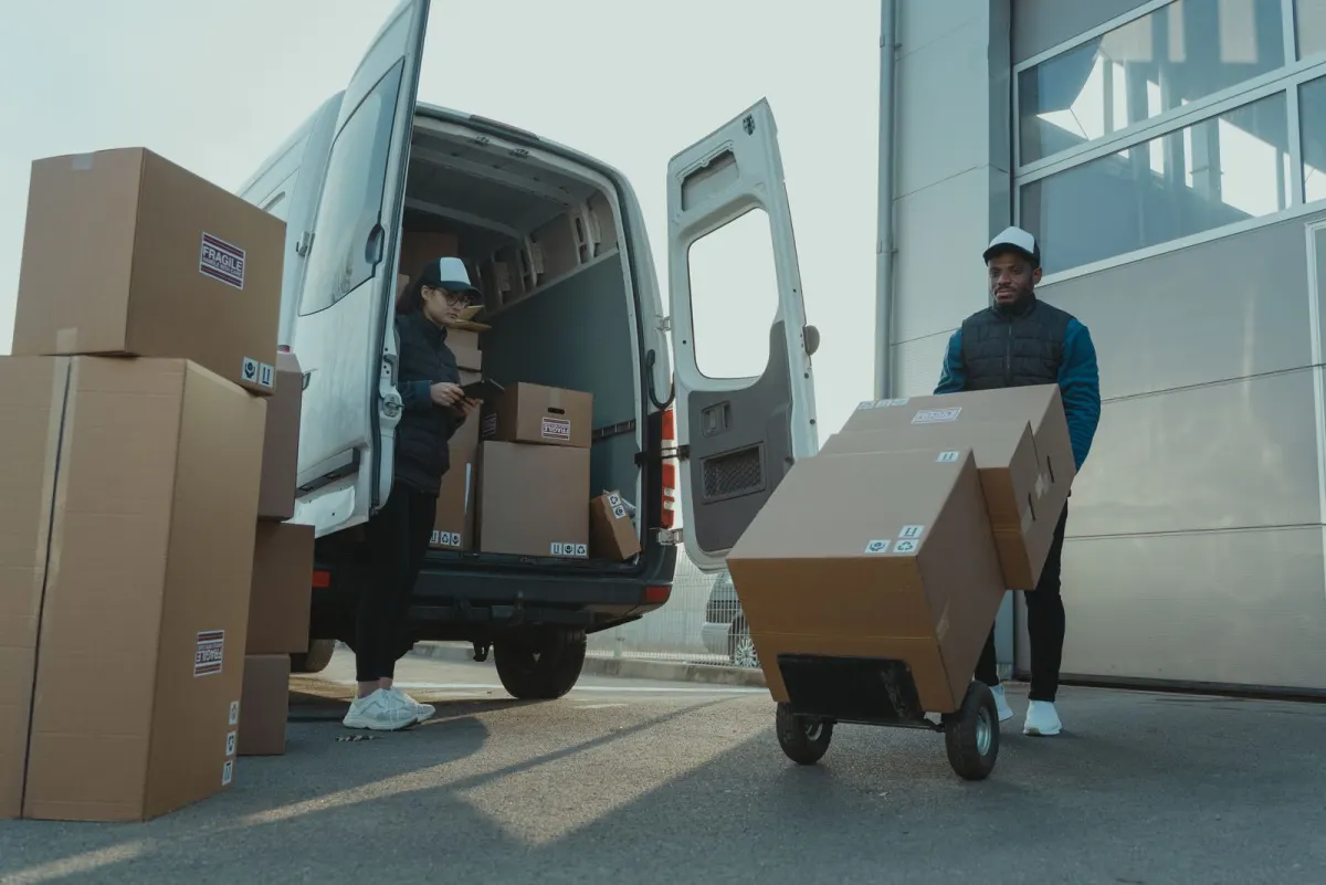 Two delivery professionals unloading boxes from a van using a hand truck