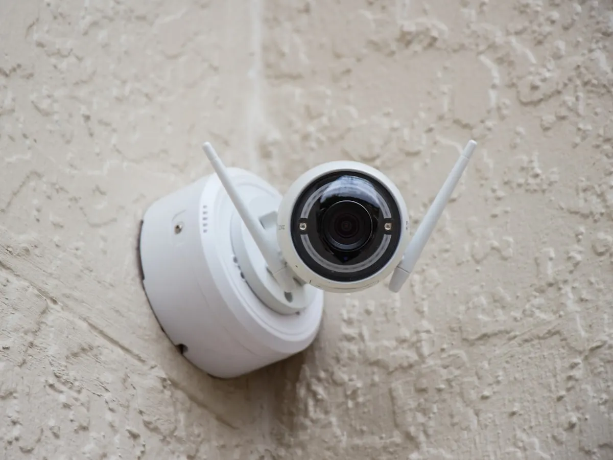 White wireless security camera neatly installed on a rendered exterior wall